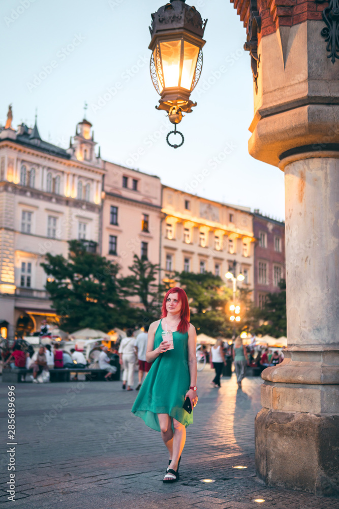 a girl with red hair holds a milk shake in her hands on the street of the old city, dressed in a green dress. Krakow Poland. Tourism food and travel. good mood, vertical photo