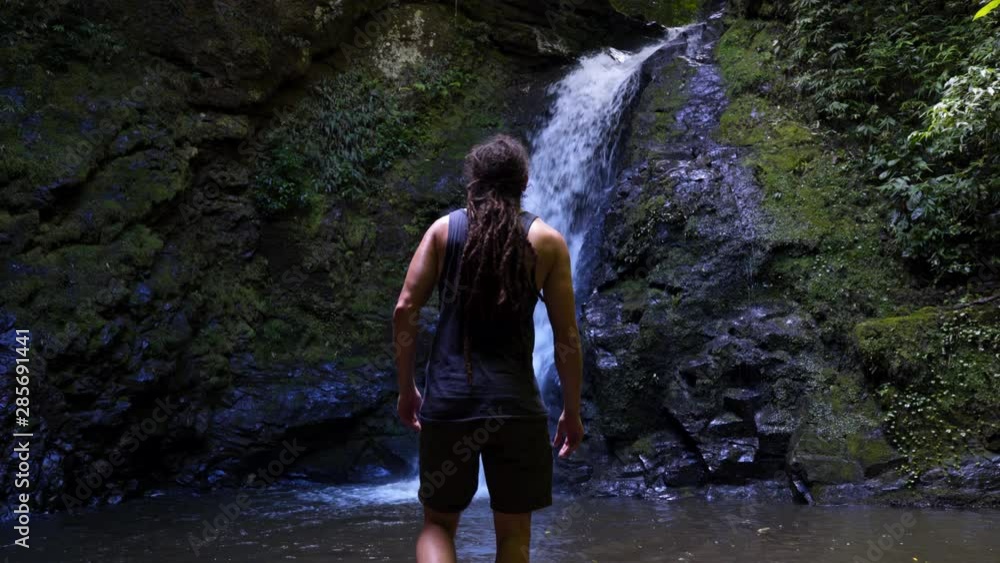 person with dreadlocks walking towards waterfall person with dreadlocks walking towards waterfall