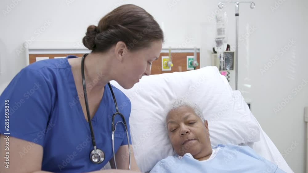 Nurse reviews information on a tablet with a patient in a hospital bed Nurse reviews information on a tablet with a patient in a hospital bed