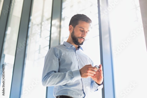 Handsome young entrepreneur using smartphone against window in office