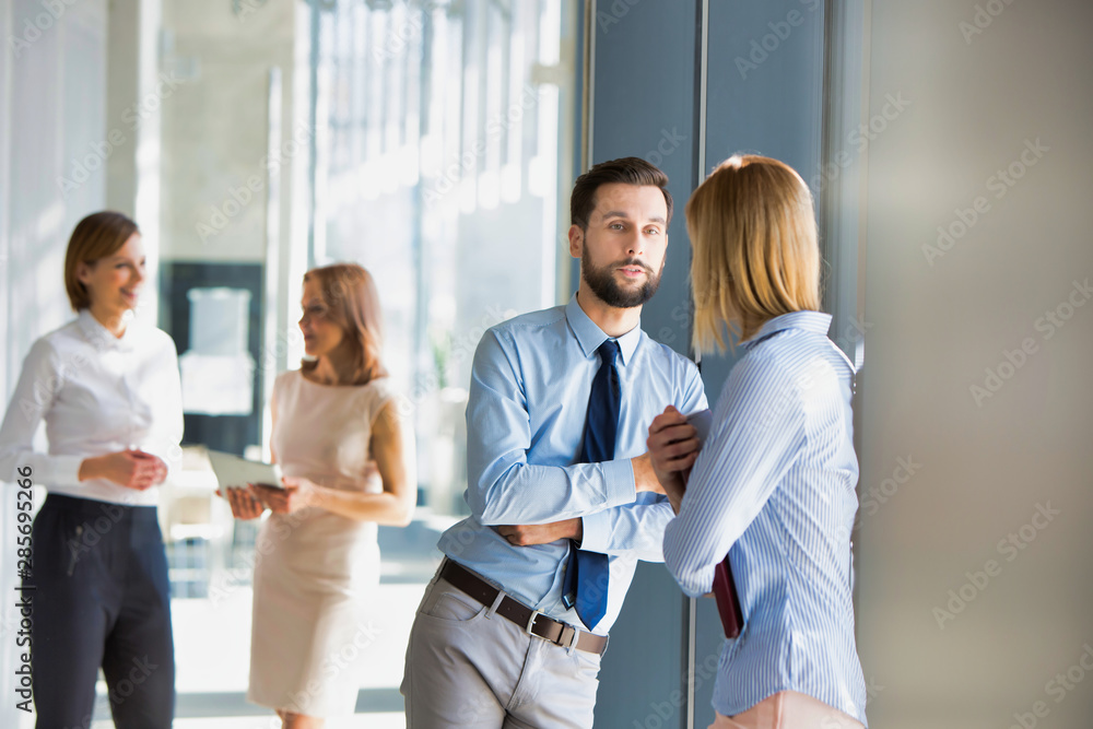 Business colleagues standing talking while leaning in office window Business colleagues standing talking while leaning in office window