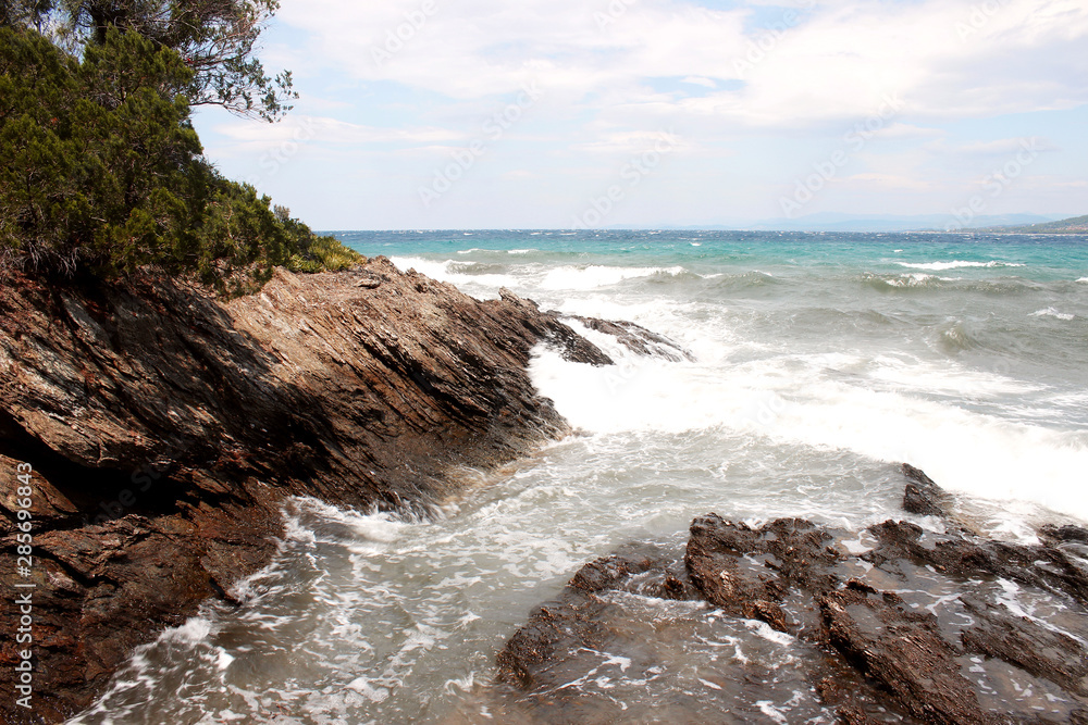 Obraz premium Waves and white foam on the sea near the rocky reef on Paradisos beach in Neos Marmaras