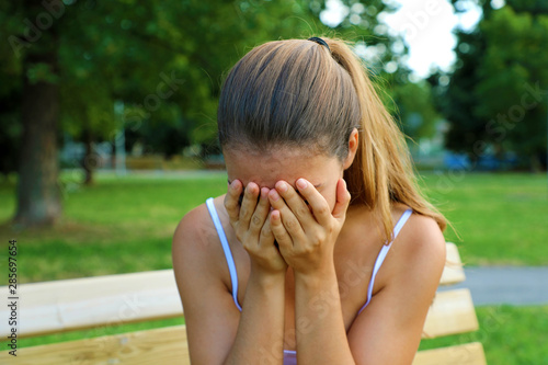 Bullying, discrimination or stress concept. Sad teenager crying alone in the park. Upset young female student having anxiety.