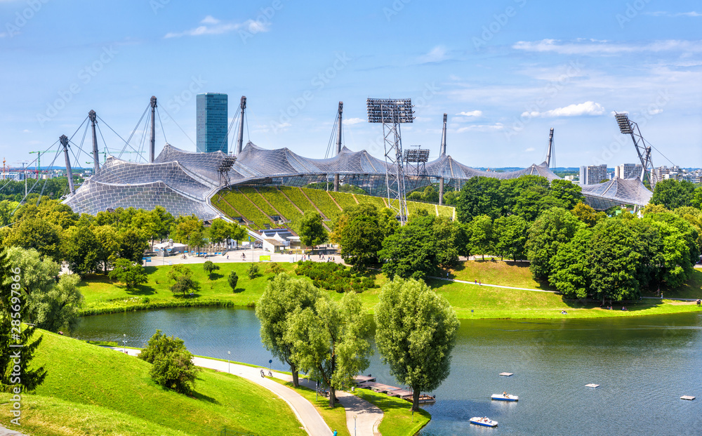 Naklejka premium Monachium Olympiapark latem, Niemcy. Malowniczy widok na stadion olimpijski i jezioro. Panorama słynnego obszaru sportowego w Monachium. Pejzaż Monachium z pięknym parkiem. Krajobraz zielonego miasta europejskiego.