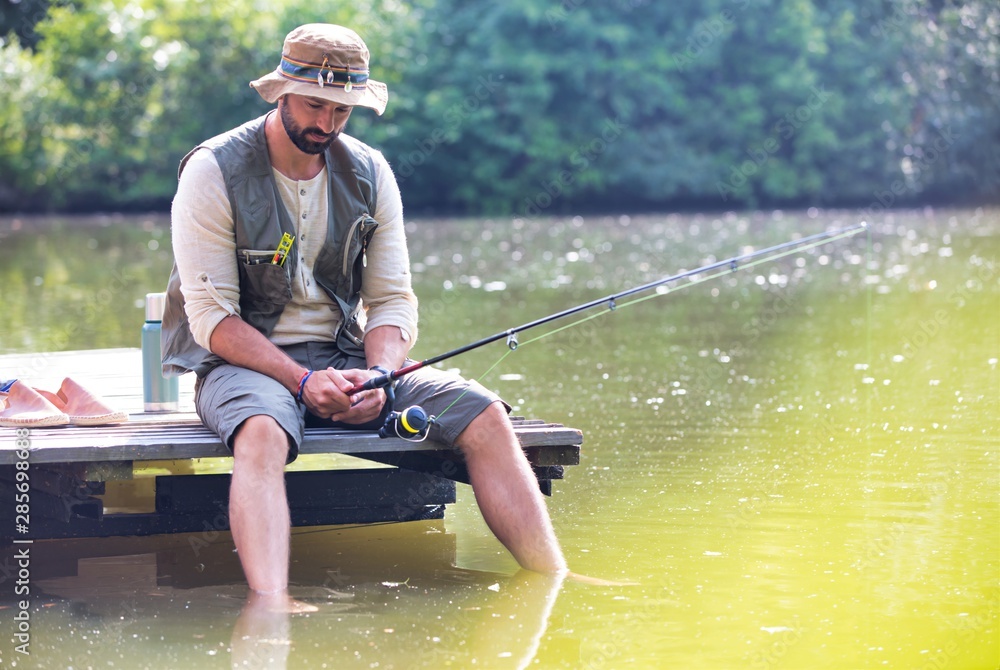 Mature man fishing in Lake while sitting on pier Mature man fishing in Lake while sitting on pier