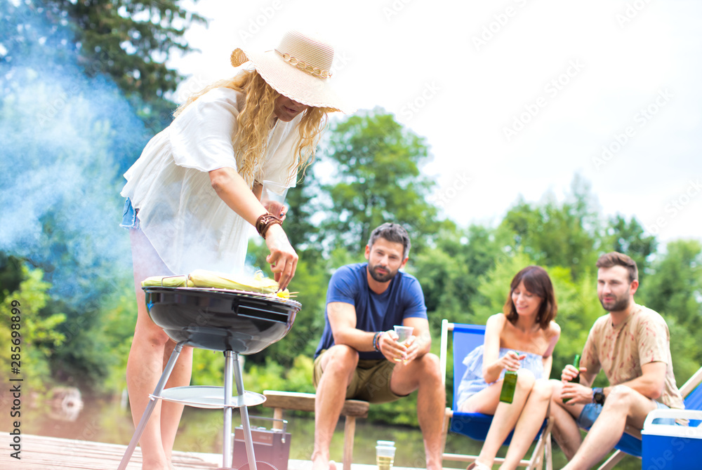 Fototapeta premium Woman preparing food in barbecue grill with friends on pier