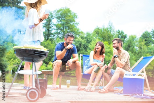 Woman preparing food in barbecue grill with friends on pier