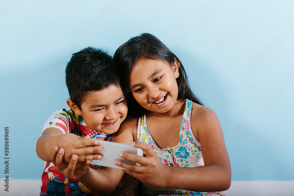 Two kids taking a selfie over blue background Two kids taking a selfie over blue background