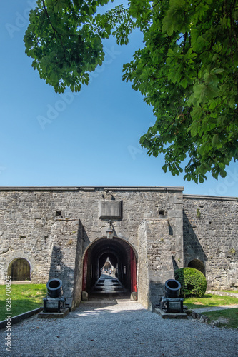 Dinant, Belgium - June 26, 2019: Inside Citadelle. Gray stoen Ramparts and gate to inner courtyard with rooms against blue sky, Green foliage. photo