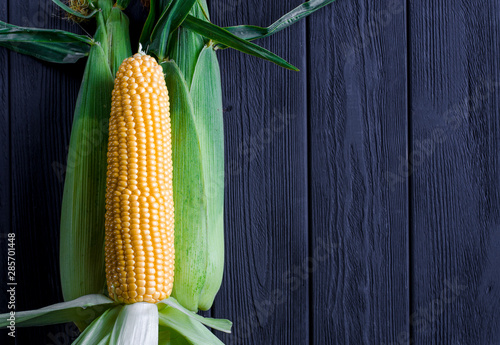 Yellow juicy corn with green leaves on a black tree table