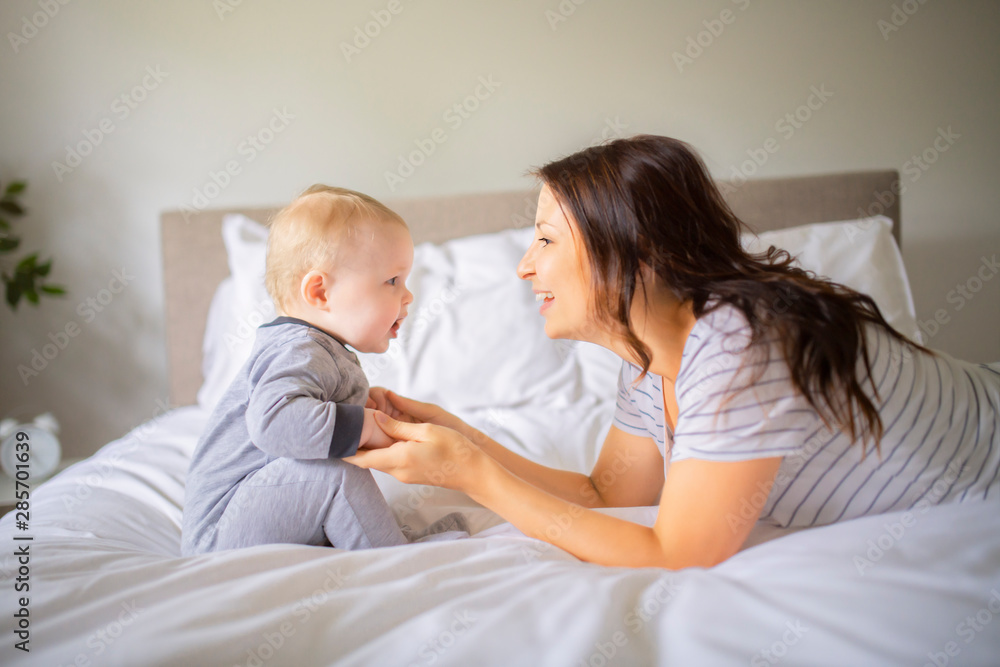 Mother and child on a white bed playing in sunny bedroom