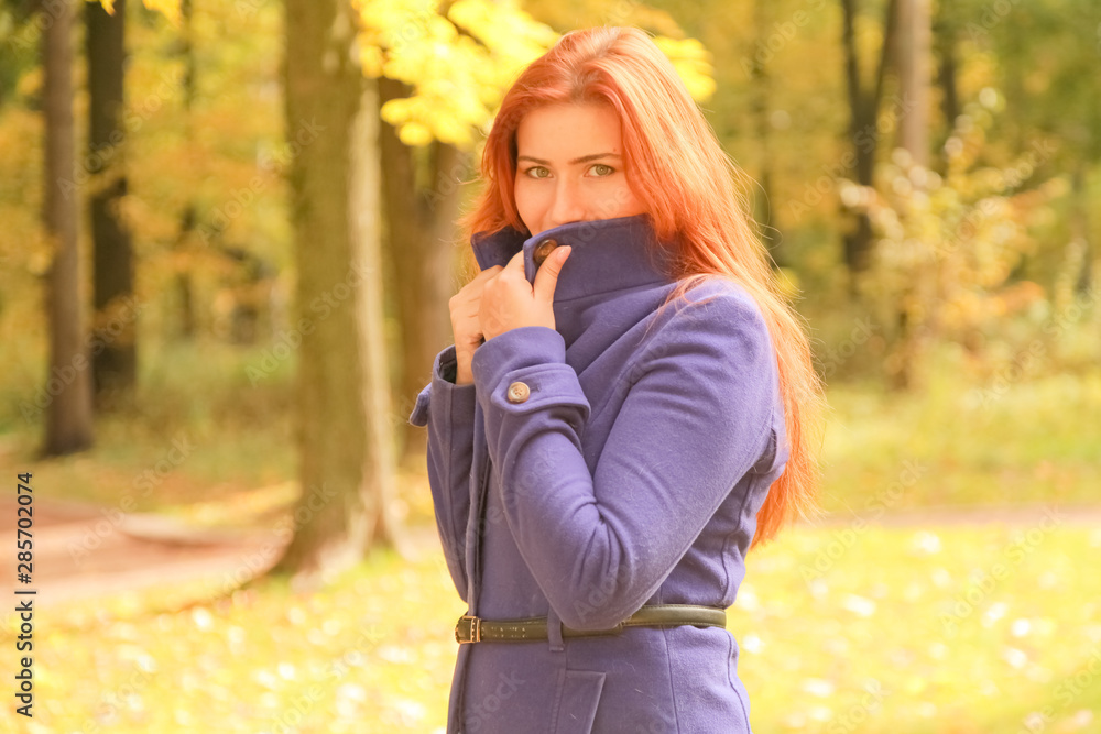 young pretty caucasian woman with red hair wearing purple jacket and walks in autumn park young pretty caucasian woman with red hair wearing purple jacket and walks in autumn park