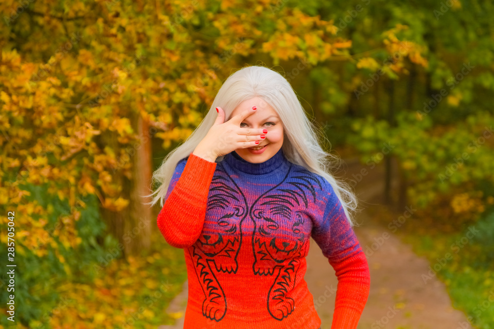 young pretty plus size caucasian woman in orange fashion sweater walks in autumn park young pretty plus size caucasian woman in orange fashion sweater walks in autumn park