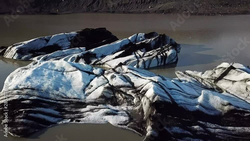 Aerial, tilt up, drone shot, panning over ice blocks, on the Jokulhlaups glacial lagoon, at Sollheimajokull Glacier, near Myrdalsjokull, on a sunny day, in southern Iceland photo