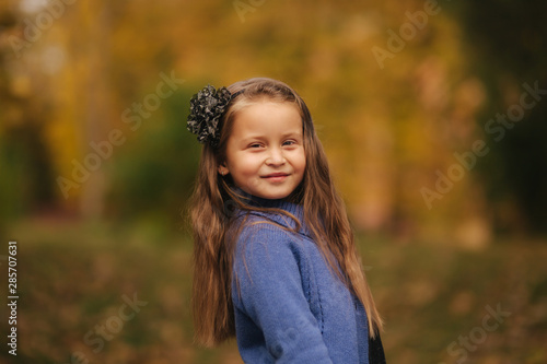 Portrait of little girl in the autumn park. Girl model poses to photographer. Happy child