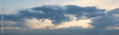 Panorama of the cloudy sky illuminated by the rays of the setting sun
