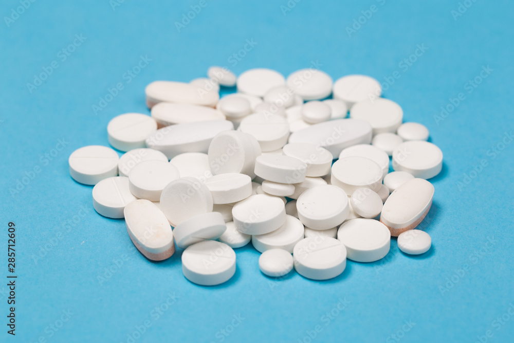 White Pills are scattered over a blue background. Close up. Medical background. White Pills are scattered over a blue background. Close up. Medical background.