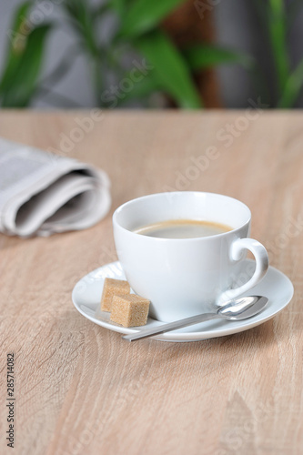 A cup of coffee and a newspaper on a table in a cafe. Light background. Free space for text.