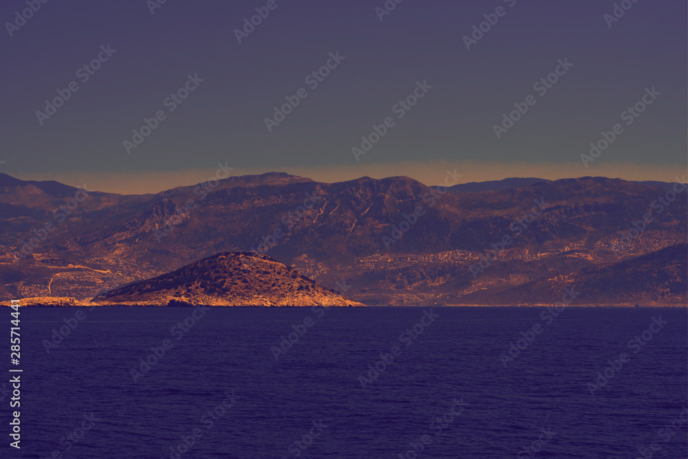 Toned background made of seascape with rocky island, mountains in mist Toned background made of seascape with rocky island, mountains in mist