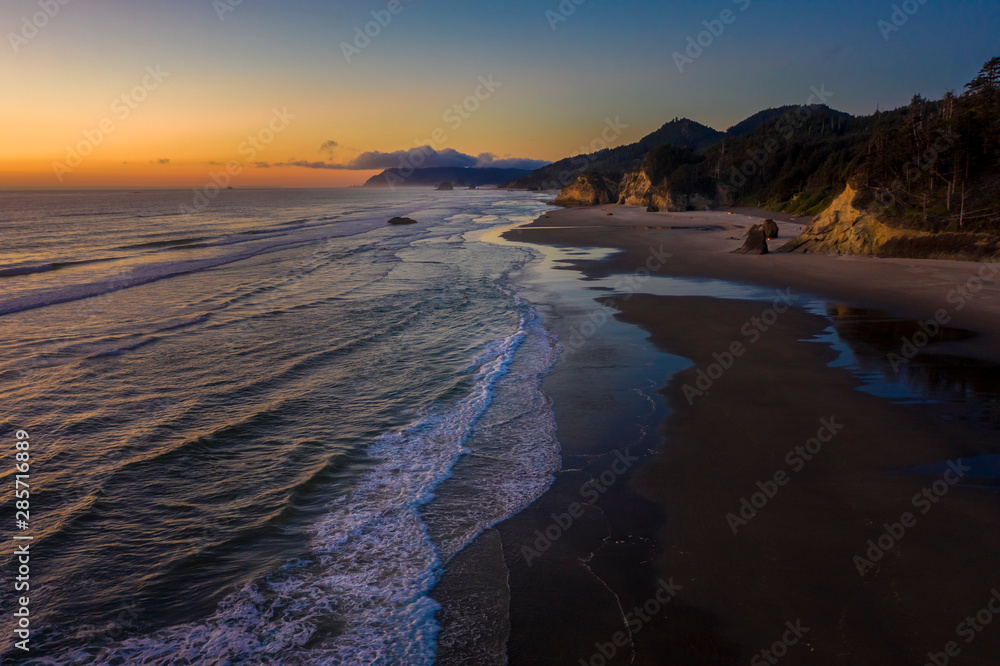 Aerial View of Arch Cape, Oregon. Sunset along the Oregon coast near Cannon Beach features white sand beaches with fir and cedar forests as far as the eye can see. 