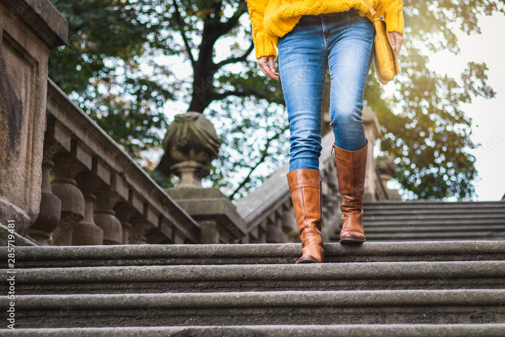 Fashion woman wearing jeans, leather boot and knitted sweater. Woman walking down ancient staircase Fashion woman wearing jeans, leather boot and knitted sweater. Woman walking down ancient staircase