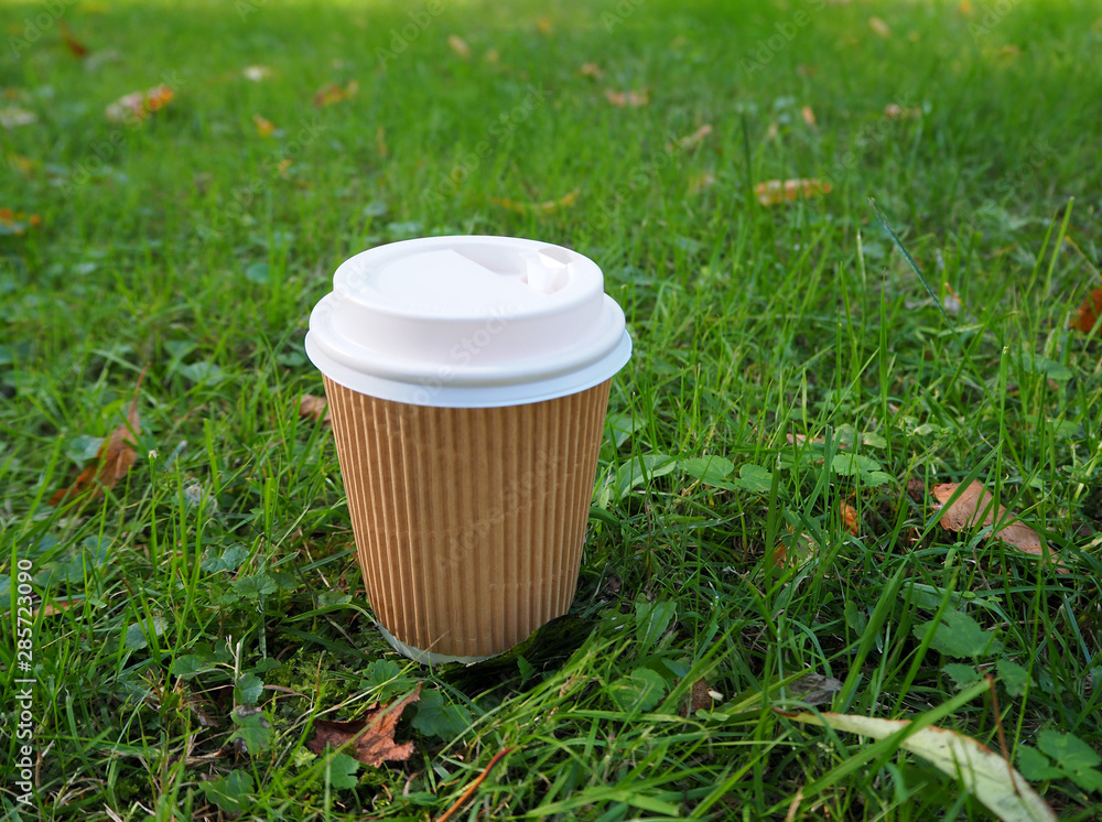 Disposable paper coffee cup on the ground among the green grass with ...