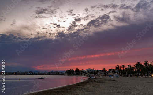 Beautiful, amazing, great sunset over the calm sea. Summer sunset over the Mediterranean Sea. Shining cloudy red and purple sky over the seacoast, sandy beach, cityscape.