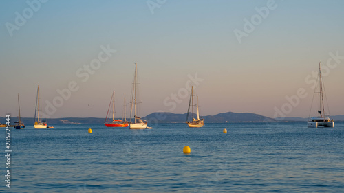 View of the bay with boats and yachts in the summer sunset on mountains and coast of the bay background. Sailing boats stay anchored in the calm sea.