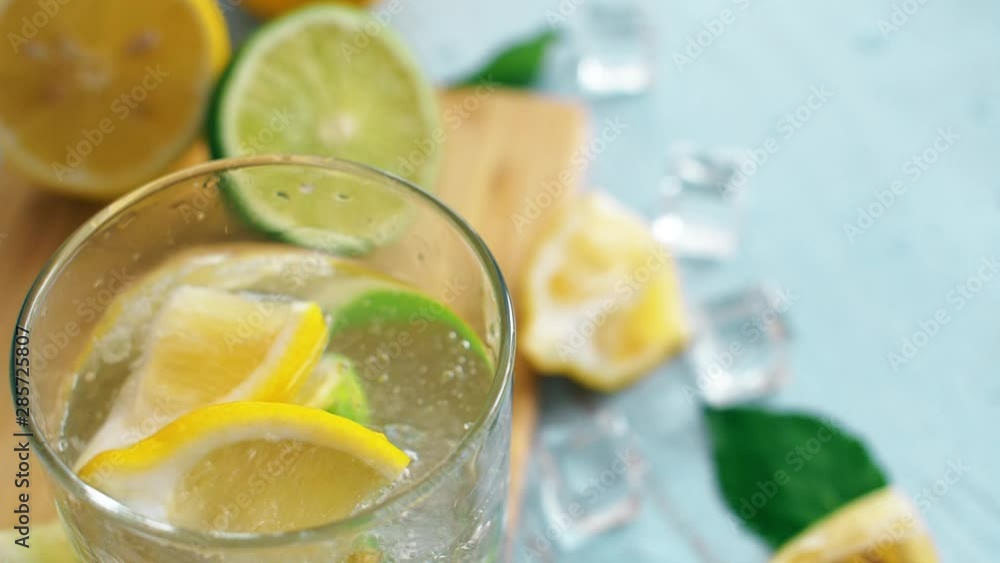 Close up slow motion sliced citrus falling intro glass with lime and lemon. Fresh coctail with ice cubes stay on chopping board. Summer drink. Close up slow motion sliced citrus falling intro glass with lime and lemon. Fresh coctail with ice cubes stay on chopping board. Summer drink.