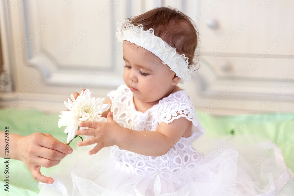 Baby girl in white dress taking a beautiful single white flower Baby girl in white dress taking a beautiful single white flower