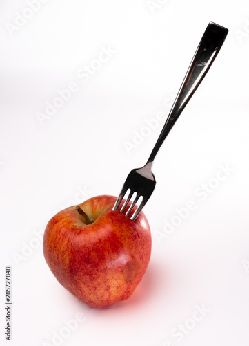 A fork is stuck in a bright red Fuji apple isolated against a white background photo