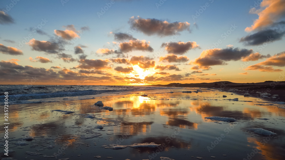Fototapeta premium Golden clouds reflecting in the sea water on the coast