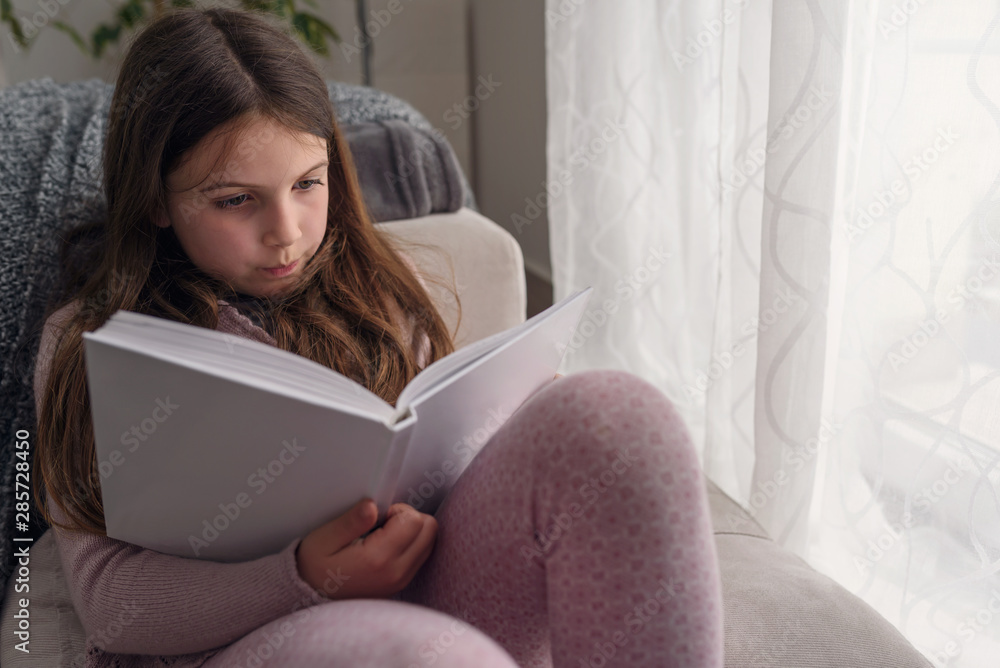 Cute little girl reading a book, at home by the window. Early reading. Cute little girl reading a book, at home by the window. Early reading.