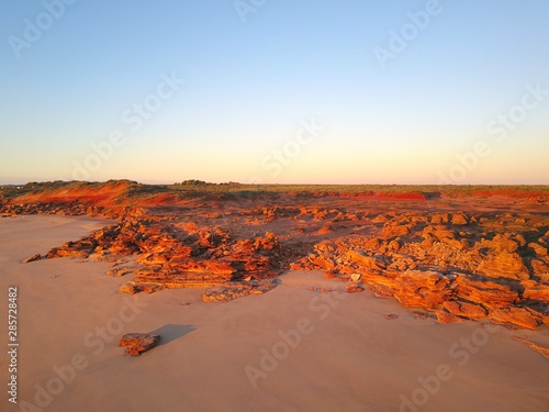 Scenic aerial panoramic view of remote coast near Broome, Western Australia, with ocean beach, red cliffs, outback landscape and sunset blue sky as copy space.