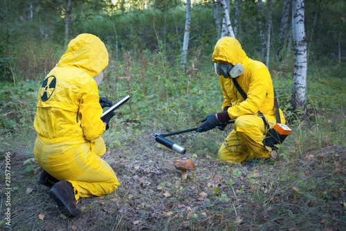 Two dosimetrist  in protective suite and mask with geiger counter measuring radiation level in danger zone