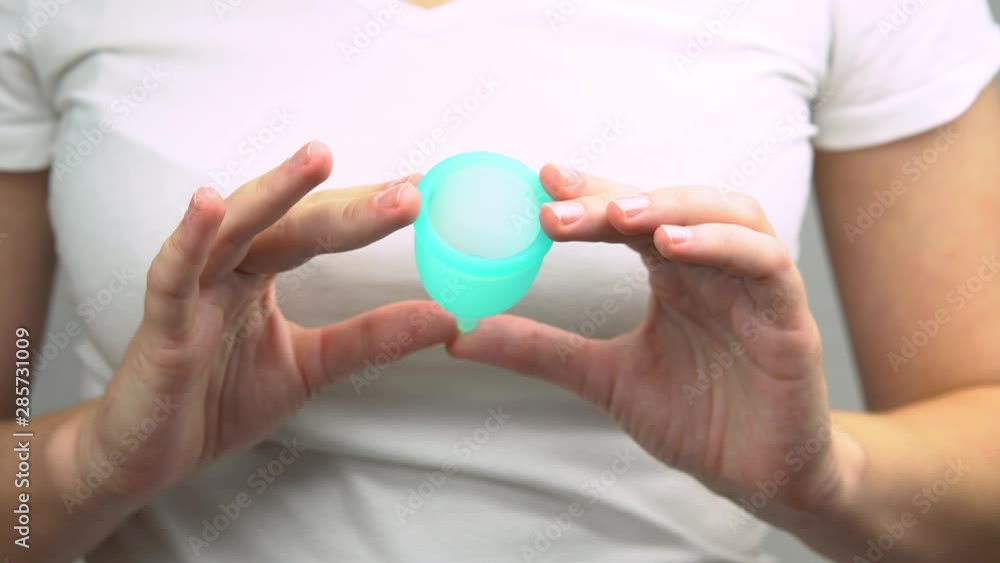 hands of a young woman demonstrate close-up blue menstrual cup, a personal hygiene product during menstruation hands of a young woman demonstrate close-up blue menstrual cup, a personal hygiene product during menstruation