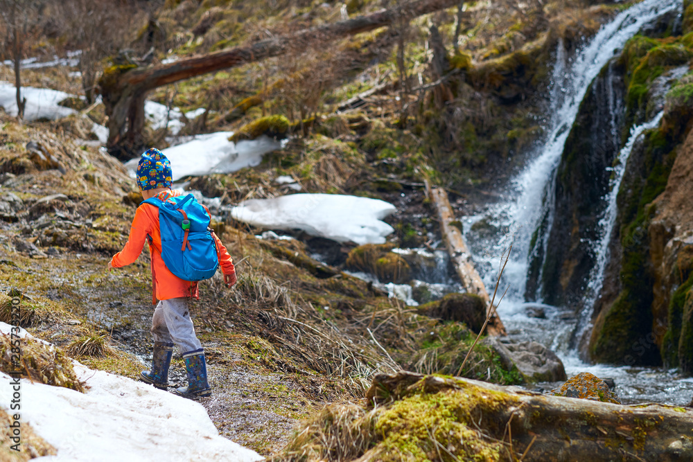 Hiking little child with backpack in hike goes near the waterfall