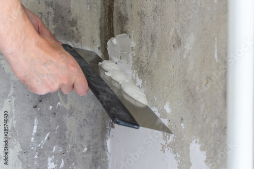 The worker covers the uneven walls, man's hands with a large spatula and putty, apartment repair