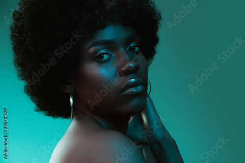 Deep ocean. Portrait of female fashion model in neon light on blue gradient studio background. Beautiful african woman with trendy make-up and well-kept skin. Vivid style, beauty, cosmetics concept.