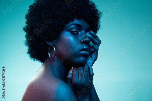 Deep ocean. Portrait of female fashion model in neon light on blue gradient studio background. Beautiful african woman with trendy make-up and well-kept skin. Vivid style, beauty, cosmetics concept.