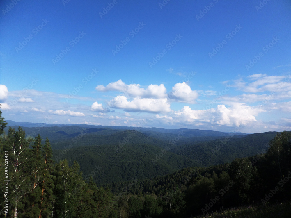 Summer landscape top view. Hills, coniferous forest and blue sky.