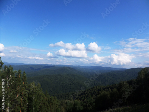 Summer landscape top view. Hills, coniferous forest and blue sky.