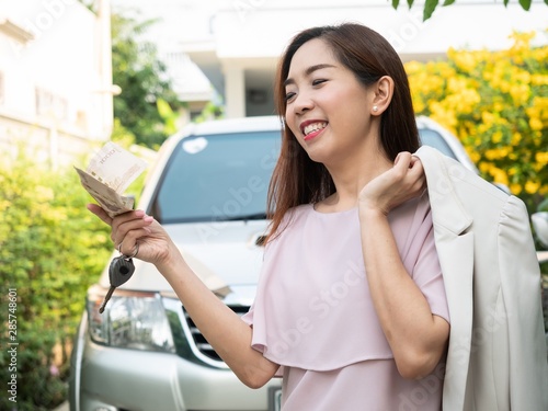 Asian woman holding money and car key against a car. insurance, loan and finance concept