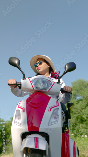 Woman on an electric scooter in the city park. Driving ecological environmentally conscious power transport. Active adult lifestyle.