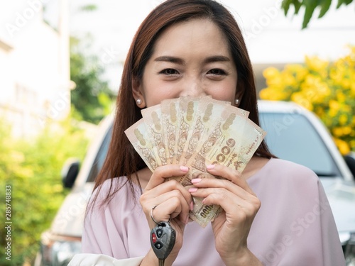 Asian woman holding money and car key against a car. insurance, loan and finance concept