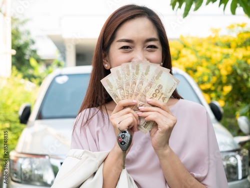 Asian woman holding money and car key against a car. insurance, loan and finance concept