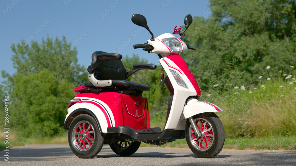 Low angle view of electric scooter on the road. Red stylish e vehicle. Environmentally  conscious transportation parked in the green city park.