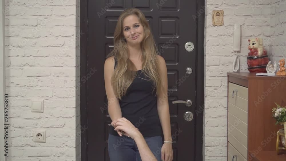 A beautiful girl is standing at the front door at home. Blonde in a black tank top and jeans. Someone hands the girl the keys to the apartment. A beautiful girl is standing at the front door at home. Blonde in a black tank top and jeans. Someone hands the girl the keys to the apartment.