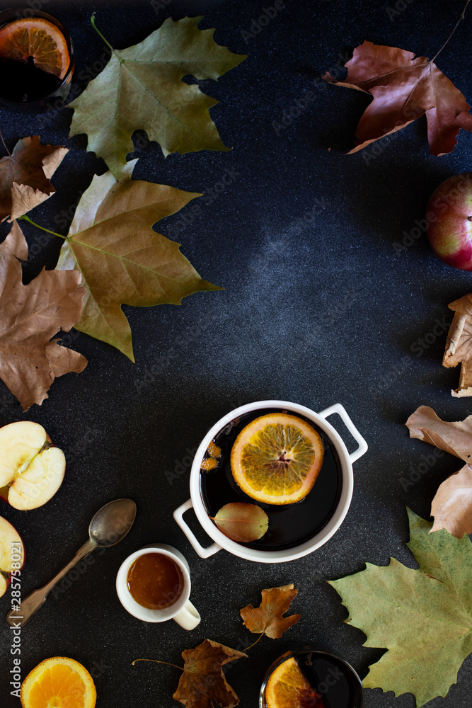 White mug with mulled wine. Autumn and winter warm alcoholic drink. Autumn leaves, honey, apples, oranges, vintage dishes. Autumn cozy mood. Flat lay, dark background. Vertical White mug with mulled wine. Autumn and winter warm alcoholic drink. Autumn leaves, honey, apples, oranges, vintage dishes. Autumn cozy mood. Flat lay, dark background. Vertical
