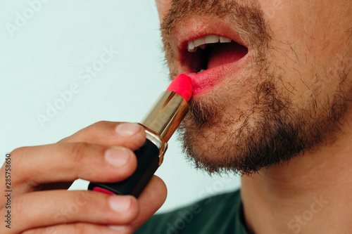 close up of a young bearded man puts red lipstick on his lips